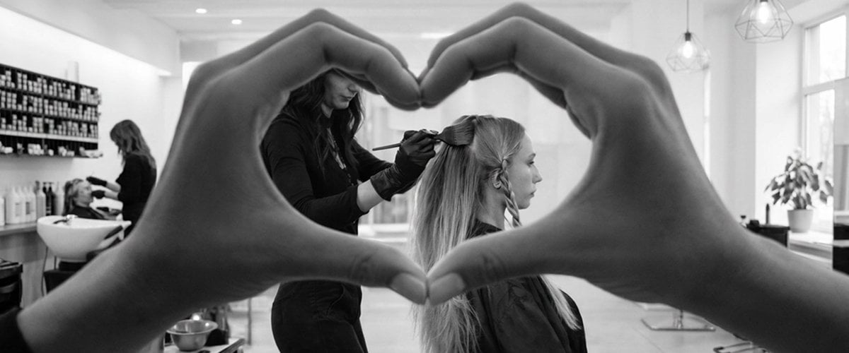 Hand heart sign with hair salon in background